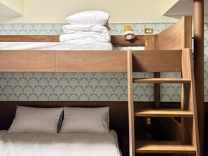 Uma cama beliche com escada de madeira, mesa de cabeceira com abajur e papel de parede estampado.