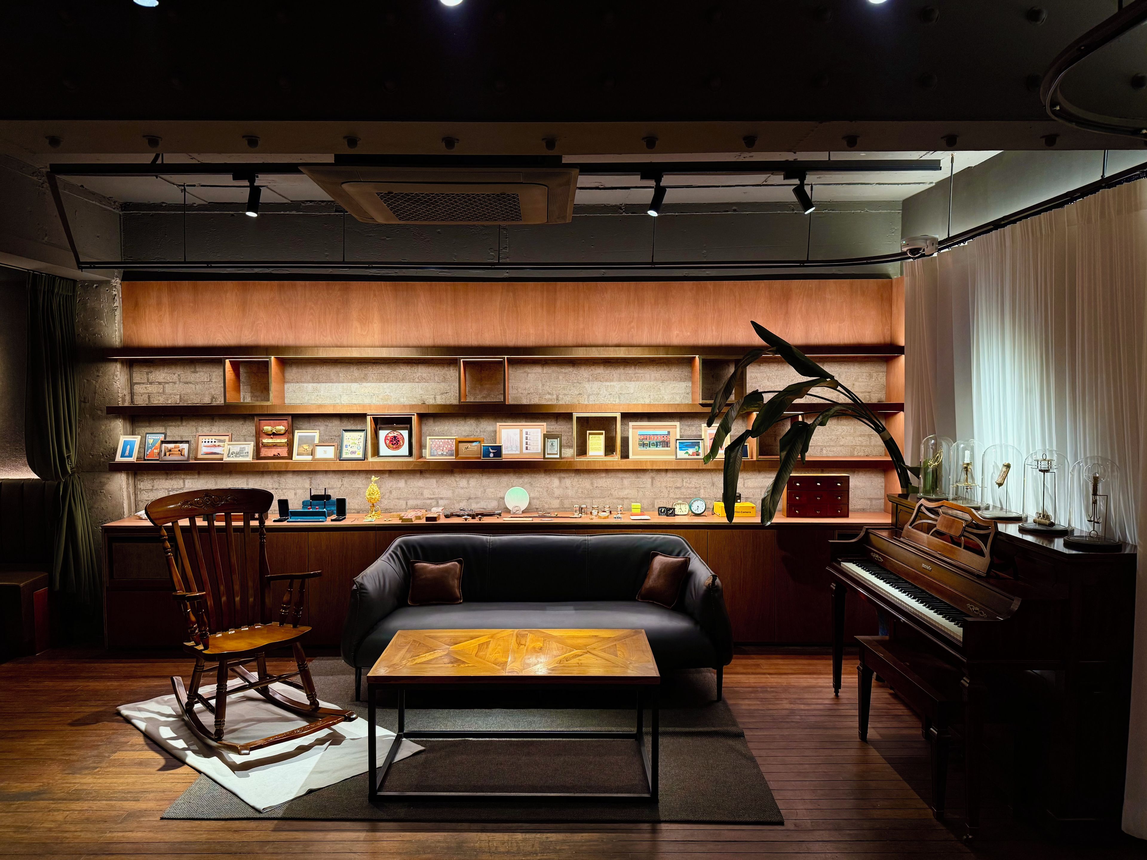 A cozy living room with a sofa, a wooden coffee table, a piano, and a bookshelf filled with framed pictures.