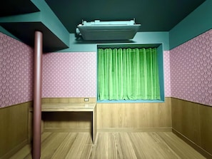 Una habitación con escritorio de madera, cortina verde, papel tapiz estampado y unidad de aire acondicionado en el techo.
