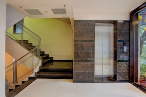 A modern interior with a staircase, a glass elevator, and a wall with a stone pattern. - Townhouse Oak Pune Railway Station (Pune)