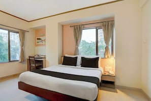 A hotel room with a large bed, a desk, and a chair. There are curtains on the windows, and a view of buildings outside. - Townhouse Oak Pune Railway Station (Pune)