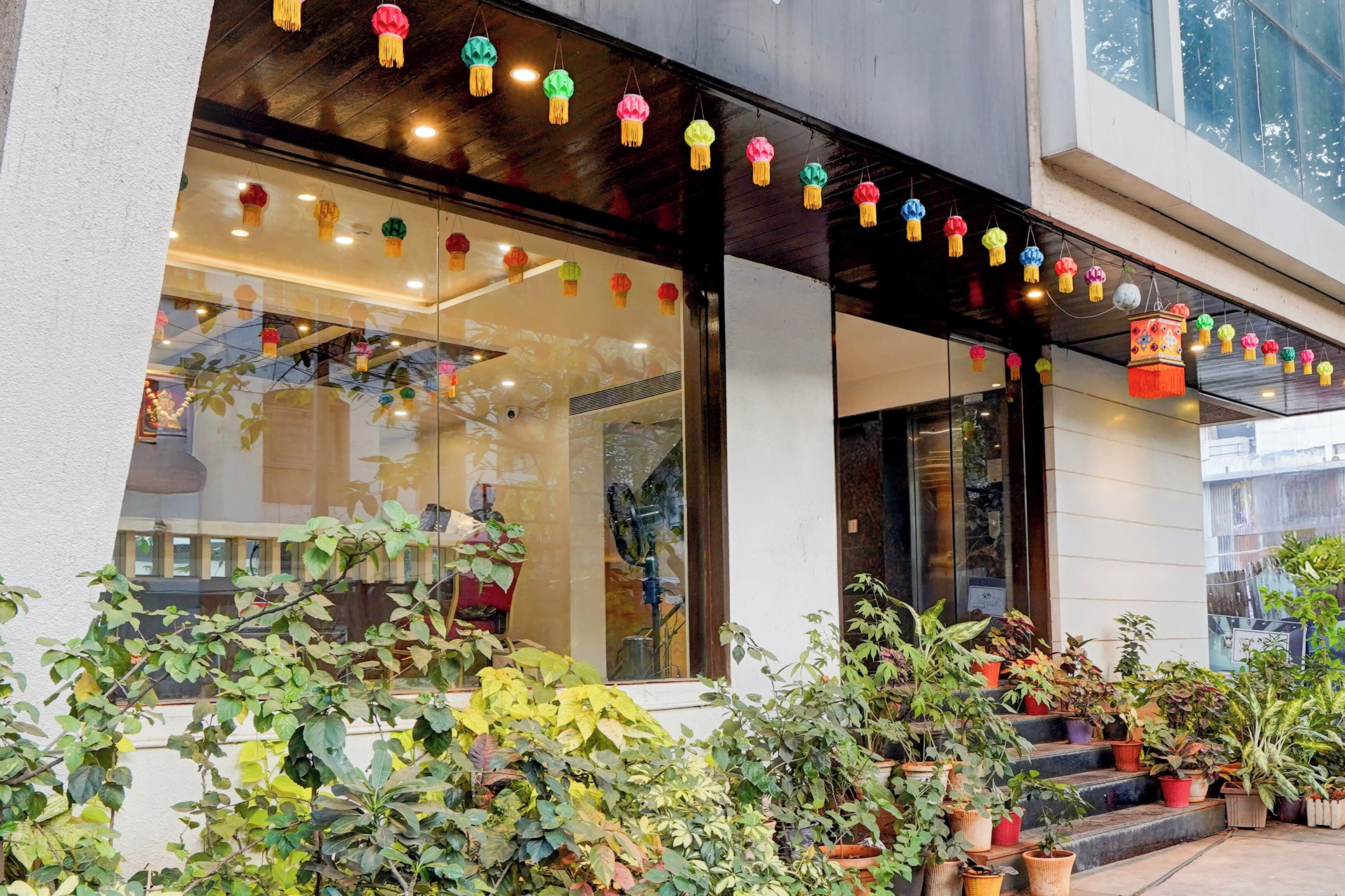 Un edifici amb grans finestres, plantes en testos a la façana i decoracions penjants de colors.
