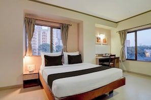 A hotel room with a bed, a desk, a chair, a nightstand, and a window with curtains. - Townhouse Oak Pune Railway Station (Pune)
