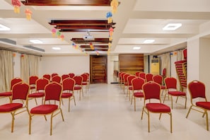 A conference room with rows of red chairs, a wooden panel wall, and ceiling-mounted projectors. - Townhouse Oak Pune Railway Station (Pune)