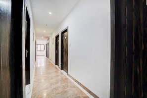 Un pasillo con puertas a ambos lados, piso de mármol e iluminación empotrada en el techo.
