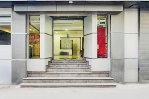 Una entrada de edificio con puerta de vidrio, un conjunto de escalones de mármol y una cortina roja a la derecha.