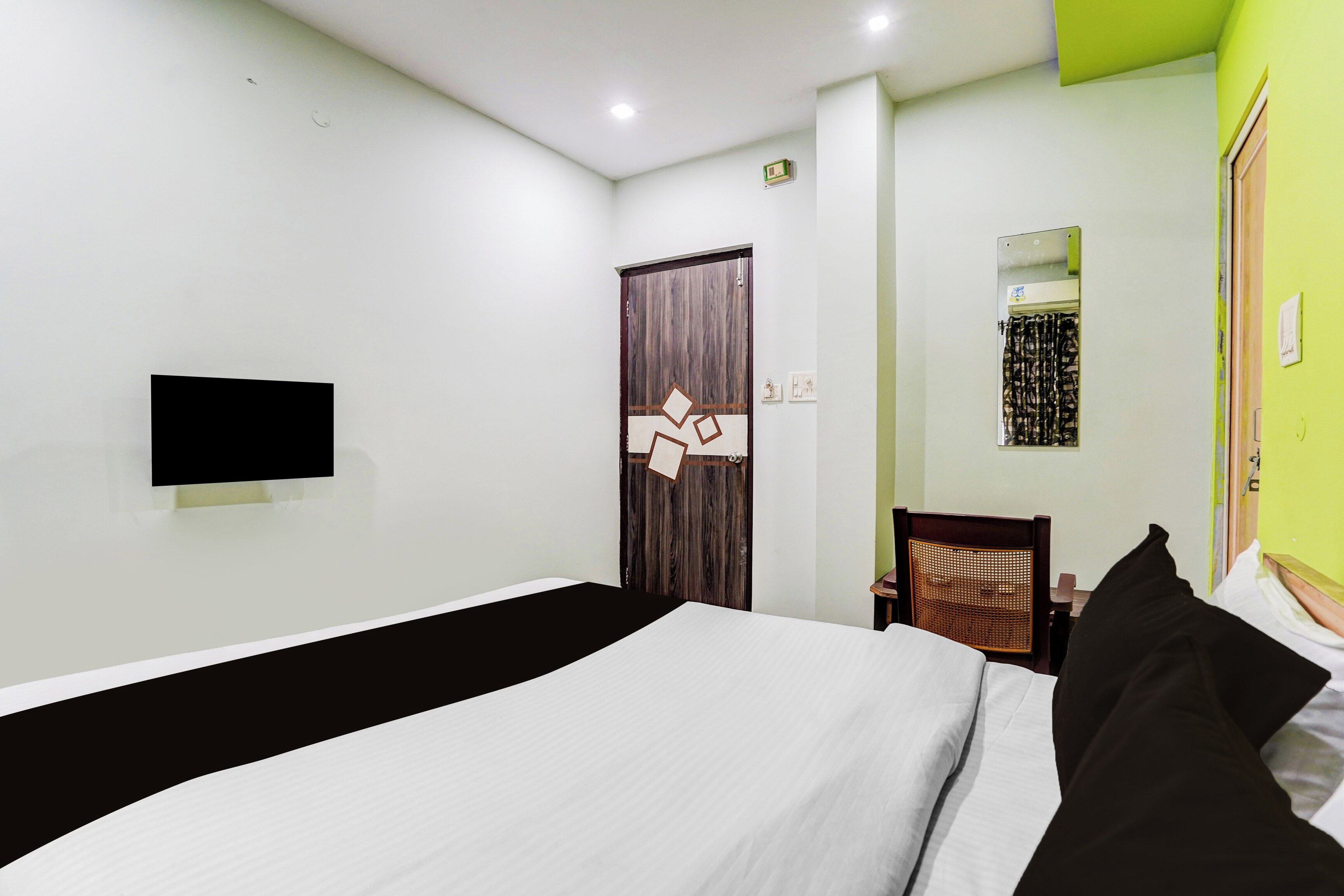 A hotel room with a bed, a television mounted on the wall, a wooden door, and a small air conditioning unit.