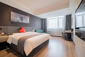Quarto de hotel moderno com uma cama grande, uma mesa de trabalho, uma cadeira e vista para a cidade pela janela.