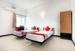Une chambre d’hôtel avec deux lits, un bureau, une chaise, une armoire et une fenêtre avec des rideaux.