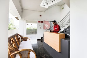 Un espace d’accueil comprenant un comptoir de réception, une réceptionniste, des fauteuils en osier, un escalier et une vue sur la ville.
