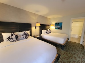 A hotel room with two beds, each with white bedding and cow-patterned pillows, a nightstand with a lamp, and a poster on the wall. - Hi-ho: A Hi-tech Hotel (Fairfield)