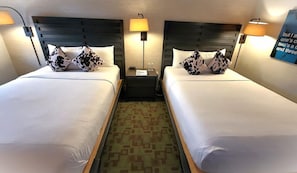 A hotel room with two beds, each with white bedding and patterned pillows, a small bedside table with a lamp, and a carpeted floor. - Hi-ho: A Hi-tech Hotel (Fairfield)