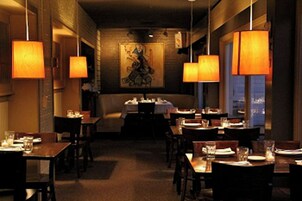 Interior de restaurante con mesas dispuestas para comer, iluminación colgante y un mural en la pared.