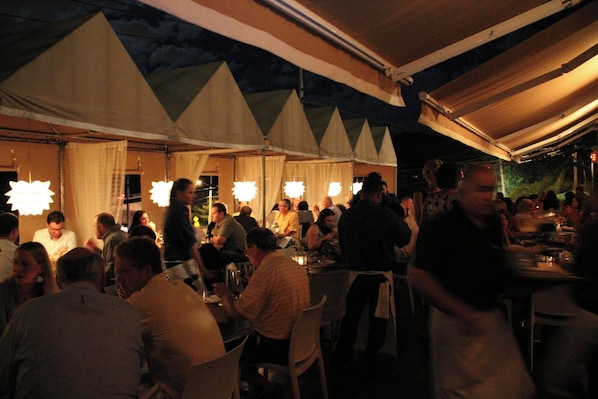 An outdoor dining area with multiple tables and chairs, under a tented roof structure. - Hi-ho: A Hi-tech Hotel (Fairfield)