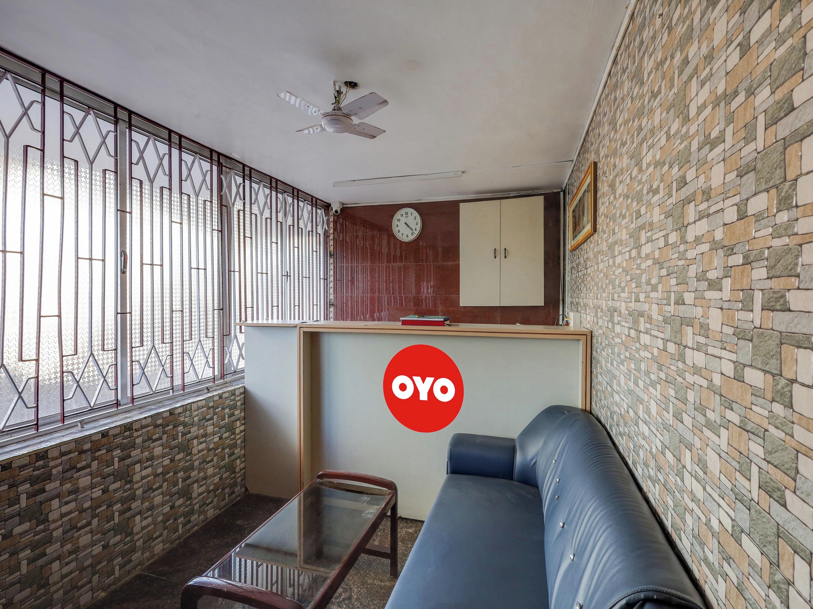 Una sala de estar con sofá, una mesa de centro de vidrio, ventilador de techo, reloj y una pared con diseño tipo mosaico.
