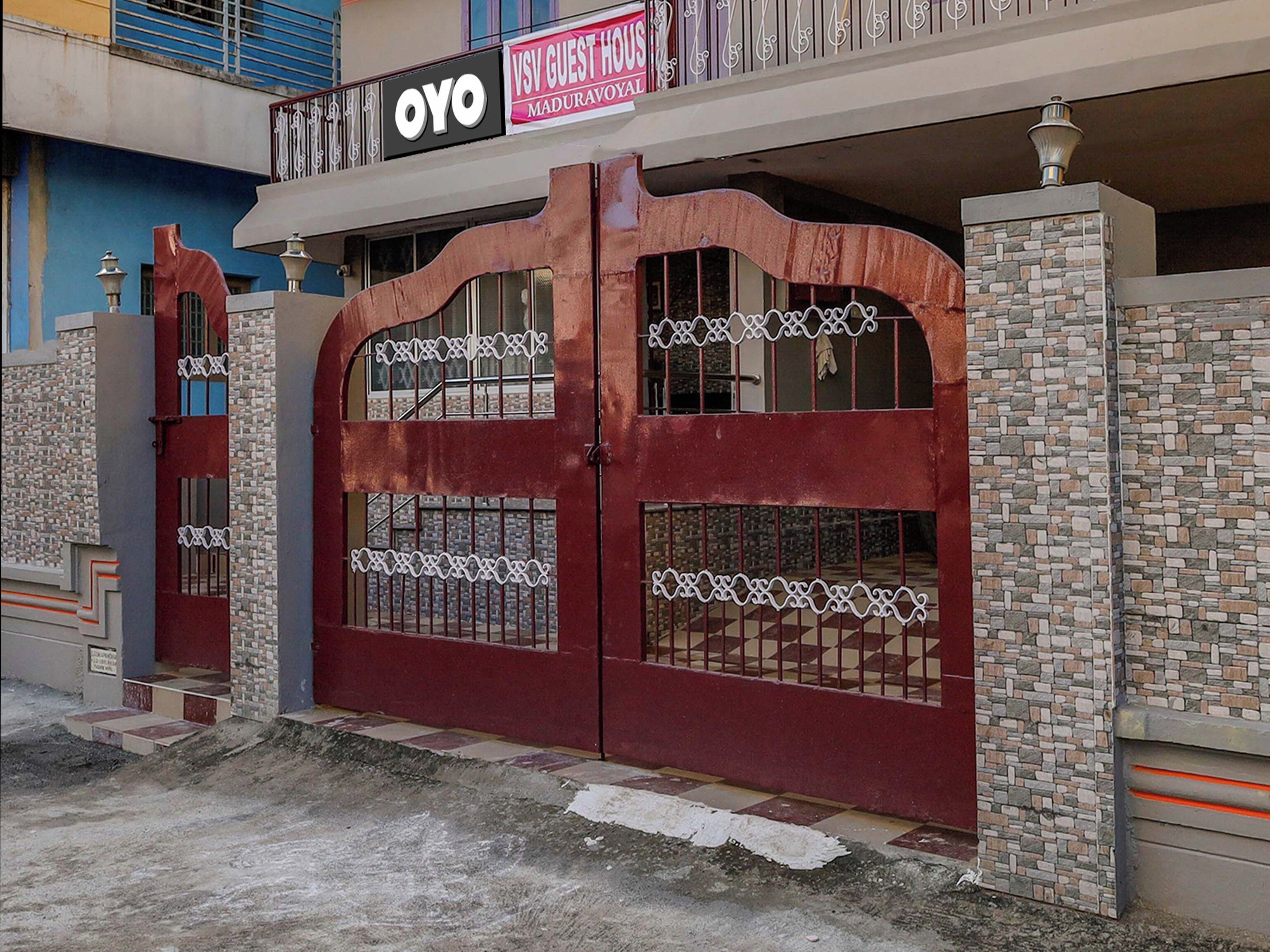 Une entrée fermée par un portail, avec une enseigne indiquant « OYO VSV GUEST HOUSE MADURAVOYA ».