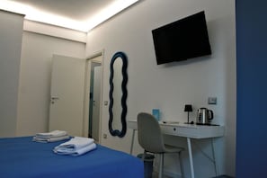 Una habitación de hotel con una cama, un escritorio, una silla, un televisor y un espejo montado en la pared.