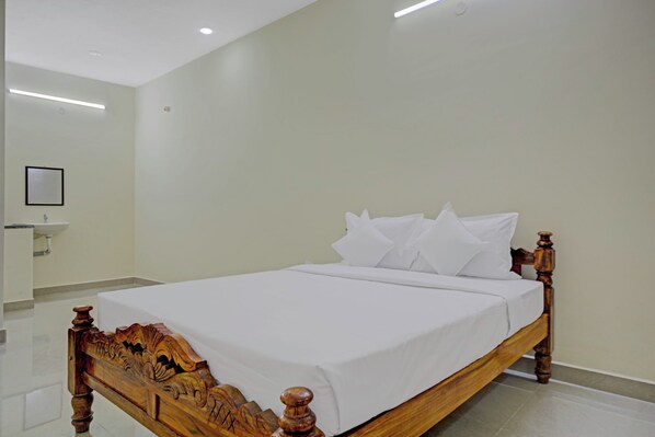 A neatly made bed in a hotel room with a wooden headboard, a white wall, and a small bedside table.