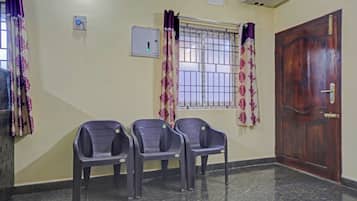A room with three plastic chairs, a wooden door, a window with metal bars, and a wall-mounted air conditioner.
