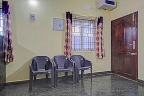 A room with three plastic chairs, a wooden door, a window with metal bars, and a wall-mounted air conditioner. - Hotel O Vsv Guest House (Chennai)