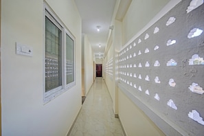 A hallway with a marble floor, a window on the left, and a wall with cloud-shaped cutouts on the right. - Hotel O Vsv Guest House (Chennai)