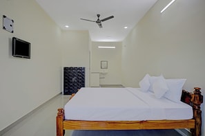 A hotel room with a bed, a television, a ceiling fan, and a bathroom with a sink.
