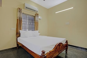 A single bed with a wooden headboard and white bedding in a room with beige walls and a tiled floor. - Hotel O Vsv Guest House (Chennai)