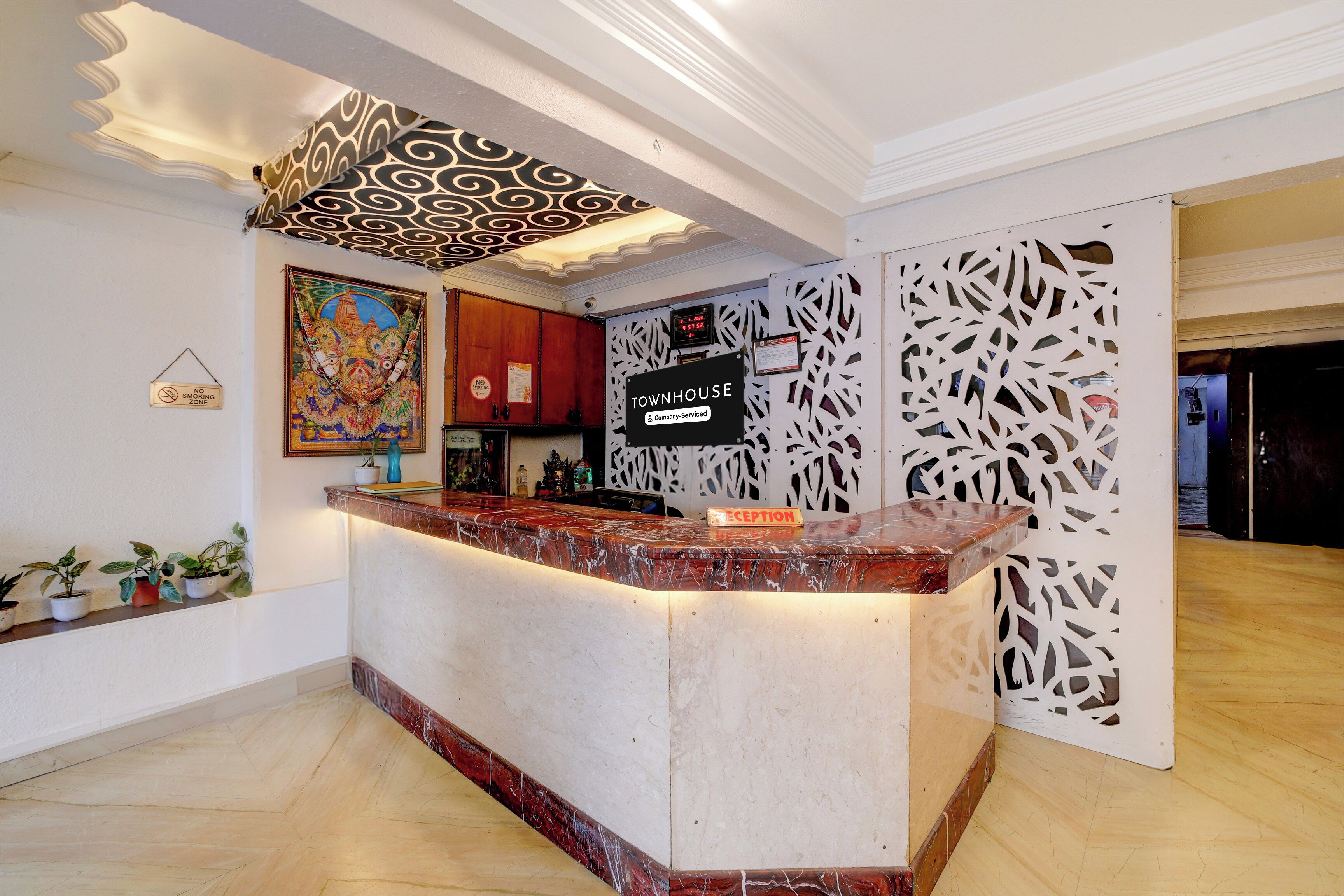 A hotel reception area with a marble counter, a 'No Smoking' sign, a 'Reception' sign, and a decorative wall panel.
