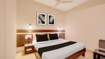 Habitación de hotel con cama, mesita de noche, florero con flores, ventilador de techo y dos cuadros en la pared.