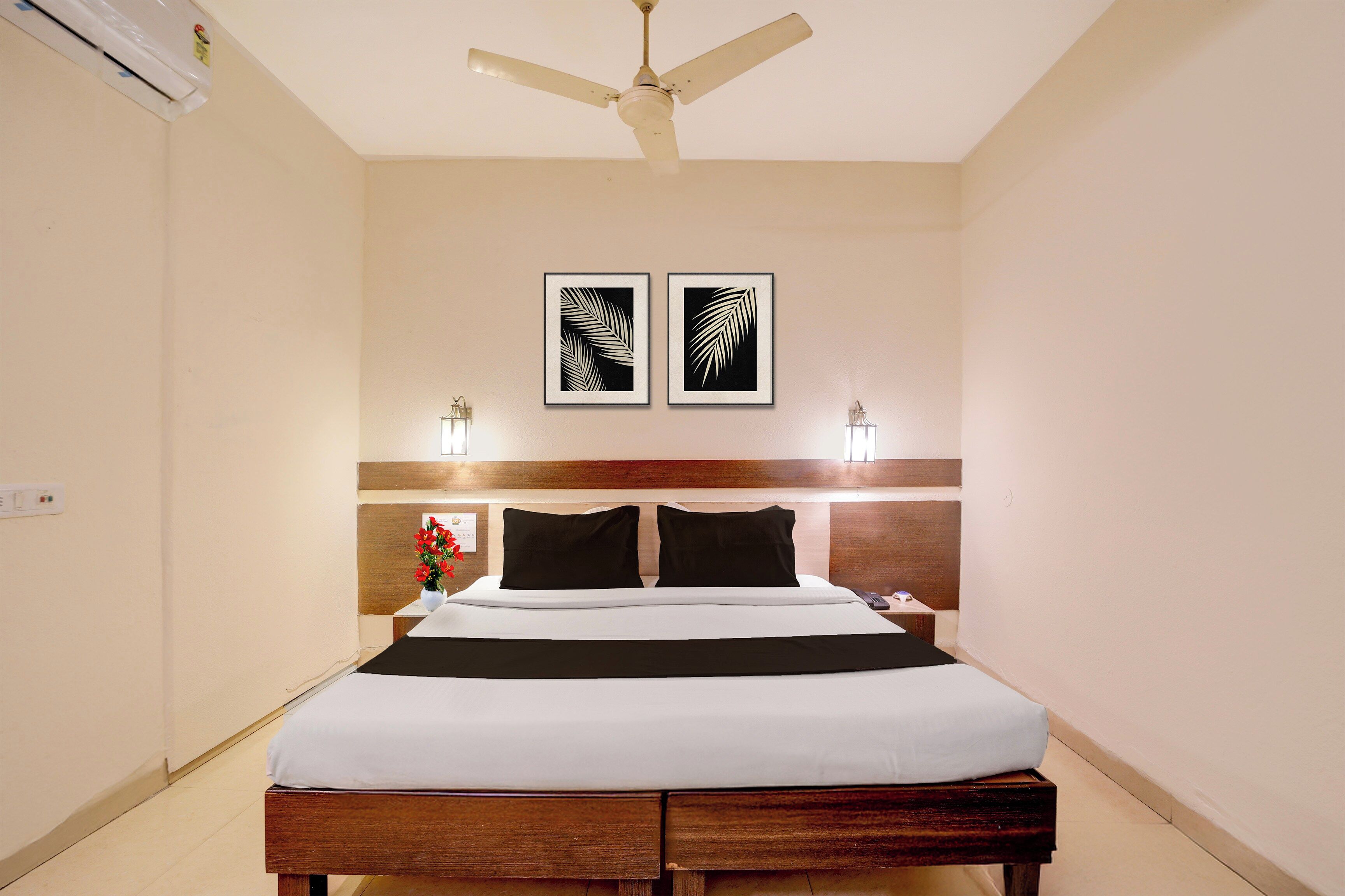 A hotel room with a bed, a ceiling fan, two wall-mounted lights, and two framed leaf designs.