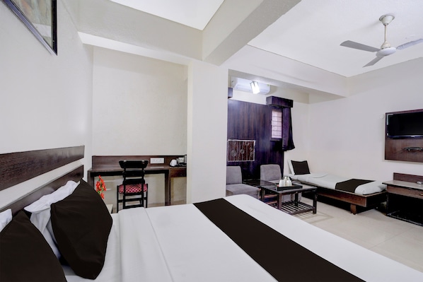 A hotel room with a bed, a desk, a chair, a television, and a ceiling fan.