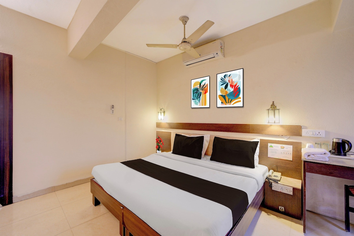 A hotel room with a bed, bedside table, a desk with a kettle, and a ceiling fan.