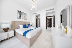 A modern hotel room with a large bed, a bedside table, a lamp, a painting on the wall, and a bathroom visible through an open door. - StayShort - Stylish 1-Bedroom Apartment in Al Furjan with Pool and Gym (Al Furjan)