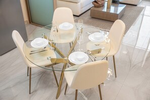 Une table ronde en verre, accompagnée de quatre chaises, chacune étant munie d’une assiette blanche et de couverts.