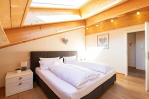 A bedroom with a skylight, a bed with white linens, a bedside table with a lamp, and a wall-mounted heart decoration. - Holiday apartment with 1 bedroom (Garmisch-Partenkirchen)