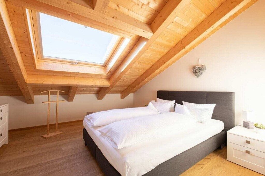 A bedroom with a sloped ceiling, a skylight, a bed with white bedding, a bedside table, and a dresser.
