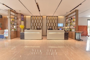 A modern hotel reception area with two reception desks, a digital screen, and a variety of amenities including a plant display and a clothing rack. - Echarm Hotel (Guilin)