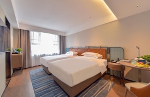A hotel room with two beds, a desk, a chair, a small table with fruits, and a window with curtains. - Echarm Hotel (Guilin)