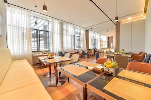 A hotel dining area with multiple tables and chairs, large windows with curtains, and a modern interior design. - Echarm Hotel (Guilin)
