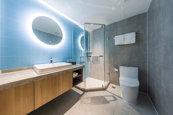 Un baño moderno con ducha envuelta en vidrio, un lavamanos con espejo y un inodoro.
