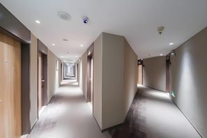 Un largo y estrecho pasillo de hotel con puertas a ambos lados, iluminación empotrada y suelo alfombrado.