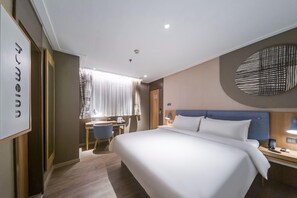 Ein Hotelzimmer mit einem großen Bett, einem Schreibtisch, einem Stuhl und einem Fenster mit Vorhängen.