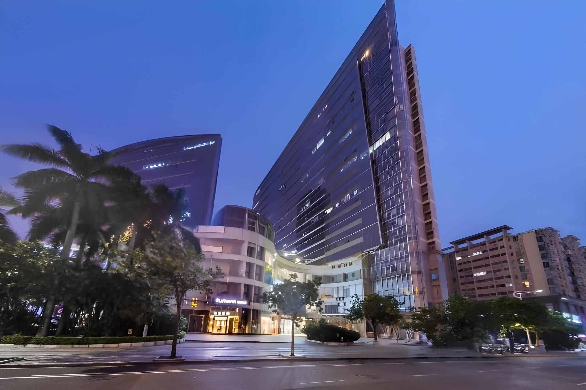 A modern urban building complex with multiple high-rise structures, a curved building, and a well-lit street.