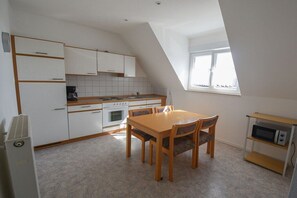 A compact kitchen with white cabinets, a wooden dining table, and a microwave on a shelf. - Holiday apartment with 2 bedrooms (Impflingen)