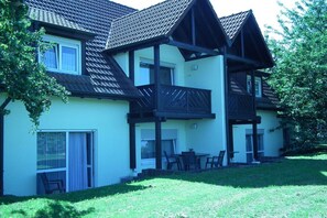 A two-story house with a balcony, a sliding glass door, and a small patio area with outdoor furniture. - Holiday apartment with 2 bedrooms (Impflingen)