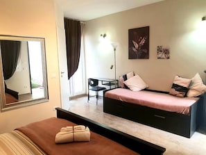 Un dormitorio con cama, escritorio y silla. Hay un espejo en la pared y una ventana con cortinas.