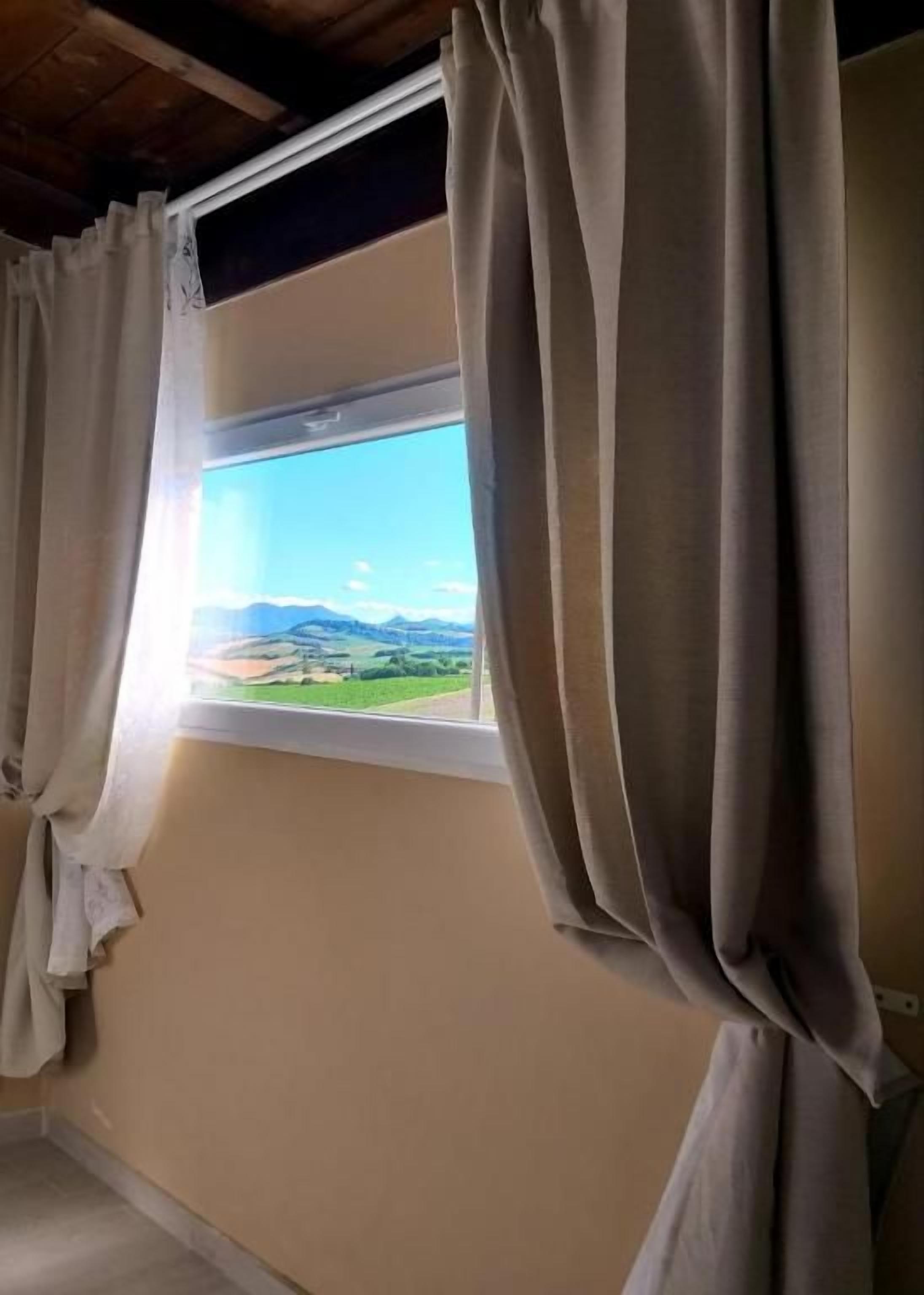 Ein Zimmer mit Fenster, Vorhängen und Blick auf eine Landschaft.