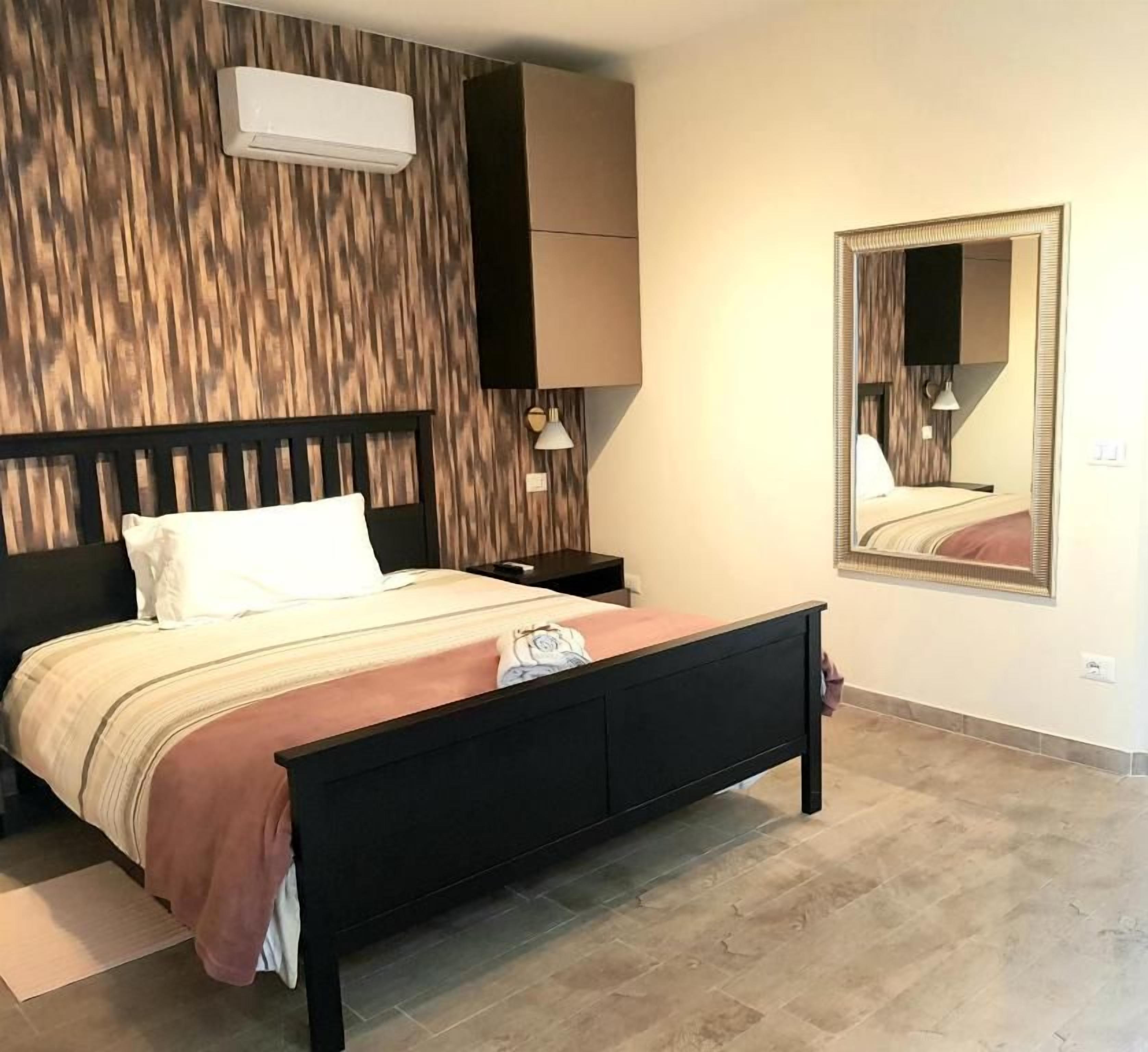 Une chambre à coucher comprenant un lit, une table de chevet, un climatiseur fixé au mur et un miroir.