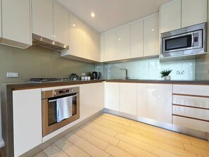 A modern kitchen with white cabinets, a stainless steel oven, a microwave, and a gas stove. - Light Filled Zetland Retreat (Zetland)