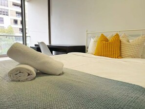 A neatly made bed with a rolled white towel, a grey blanket, and a white headboard. - Light Filled Zetland Retreat (Zetland)